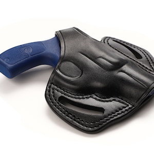 Könnte beinhalten: Schwarze Lederholster mit einer blauen Handfeuerwaffe. Die Holster hat ein geformtes Design mit genähten Kanten und Aussparungen. Der Griff der Handfeuerwaffe ist blau, und der Lauf befindet sich im Inneren der Holster.