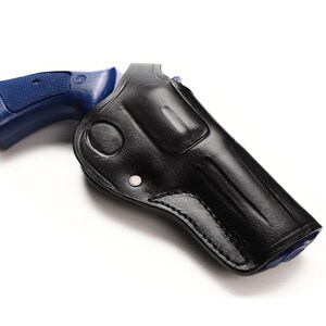 Op de afbeelding: Een zwarte leren holster met een blauwe pistoolgreep. De holster is ontworpen om de vorm van het pistool te passen, met een gebogen ontwerp en een druksluiting. De achtergrond is wit.