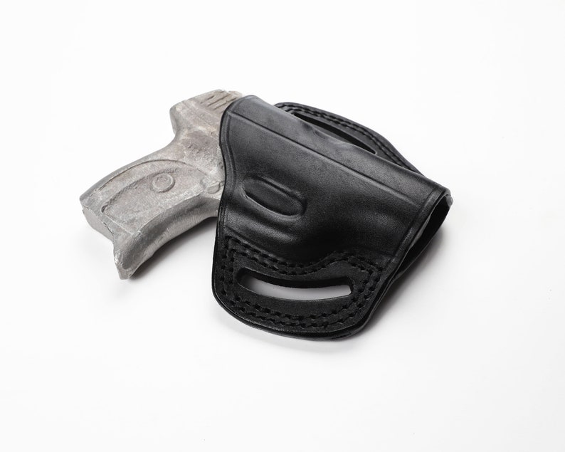 May include: A black leather holster with a stitched design. The holster is designed to hold a handgun. The image is set against a white background.