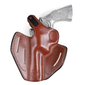 May include: A brown leather holster with a silver handgun. The holster has white stitching and a black border. The handgun is partially inserted into the holster, with the grip visible. The holster is designed to hold a firearm.