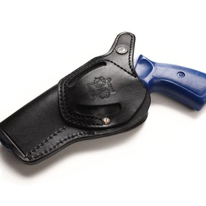 May include: A black leather holster with a blue revolver inside. The holster has a stitched design and a metal button.