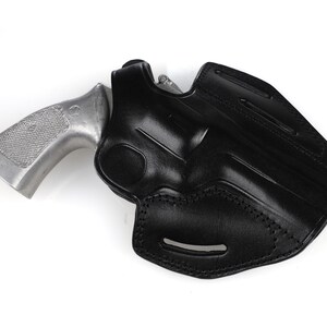 May include: A black leather holster with a silver revolver. The holster is molded to the shape of the gun and features stitching and a belt loop. The revolver has a textured grip.