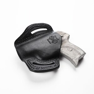 May include: Black leather holster with stitched detailing and a stamped emblem. The holster is designed to hold a handgun, visible partially inside. The background is plain white.