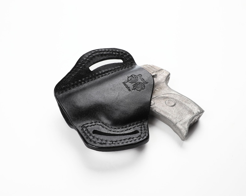 May include: Black leather holster with stitched detailing and a stamped emblem. The holster is designed to hold a handgun, visible partially inside. The background is plain white.