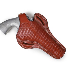 Pode incluir: Um coldre de couro marrom com um padrão tecido e costuras brancas. O coldre é projetado para segurar uma arma de fogo.