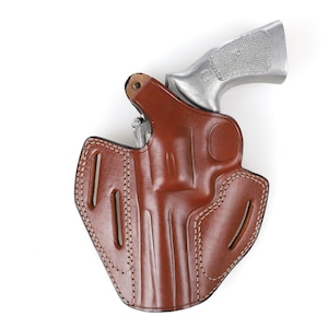 May include: A brown leather holster with a silver handgun. The holster has a molded design with visible stitching and belt loops. The handgun's grip is visible, and the overall image is set against a white background.