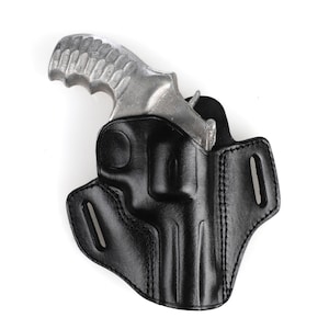 Op de afbeelding: Een zwart leren holster voor een zilveren revolver. Het holster heeft een riemlus en een drukknopsluiting.