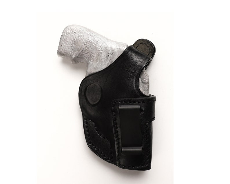 Puede incluir: Una funda de cuero negra con una pistola plateada en su interior. La funda tiene un clip para el cintur&oacute;n.