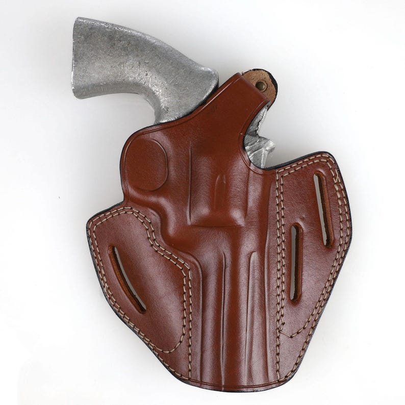 Puede incluir: Una funda de cuero marr&oacute;n con un rev&oacute;lver plateado. La funda tiene costuras decorativas y recortes. El rev&oacute;lver est&aacute; parcialmente insertado, mostrando el ca&ntilde;&oacute;n y el cilindro.