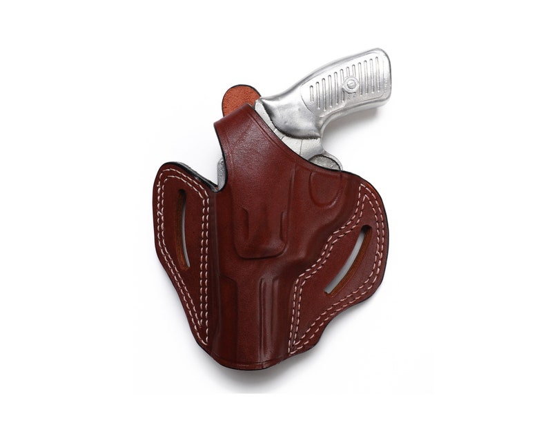Puede incluir: Una funda de cuero marr&oacute;n con costuras blancas para una pistola plateada.