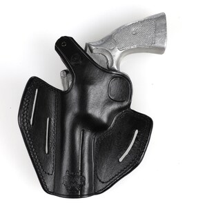 May include: A black leather holster with a silver handgun. The holster has a molded design with stitched edges and vertical slots. The handgun is partially inserted into the holster, with the grip visible.