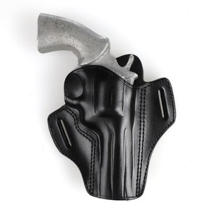 Puede incluir: Una funda de cuero negra para un revólver. La funda tiene un bucle para el cinturón y un cierre a presión.