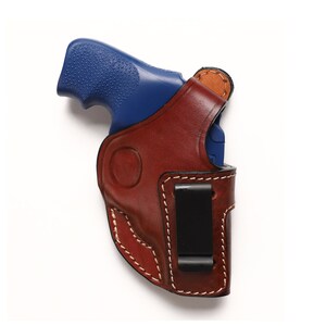 May include: A brown leather holster with a black clip for a blue handgun.