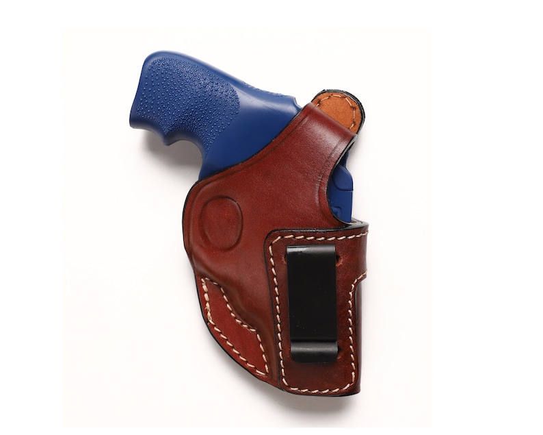 May include: A brown leather holster with a black clip for a blue handgun.
