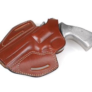 May include: A brown leather holster with white stitching, holding a silver handgun. The holster has a molded design and a belt loop. The handgun's grip is textured.