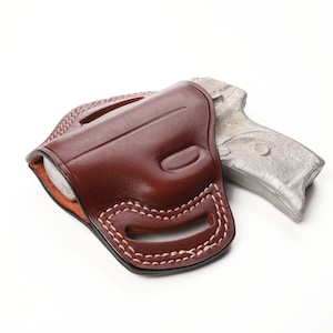 May include: A brown leather holster with white stitching, holding a silver handgun. The holster is designed to fit the shape of the gun, with a curved design and open top. The background is white.
