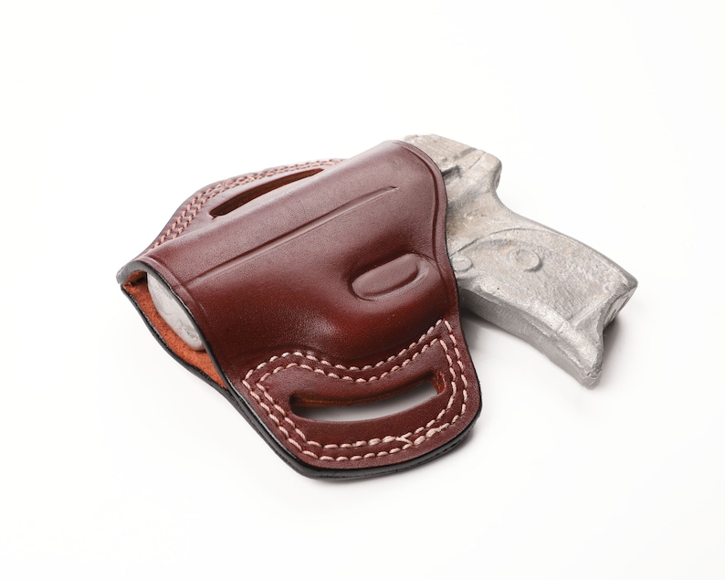 May include: A brown leather holster with white stitching, holding a silver handgun. The holster is designed to fit the shape of the gun, with a curved design and open top. The background is white.
