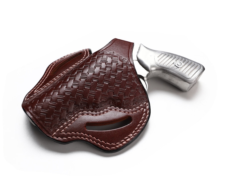 May include: A brown leather holster with a woven pattern and a stitched edge. The holster is designed to hold a small silver revolver.