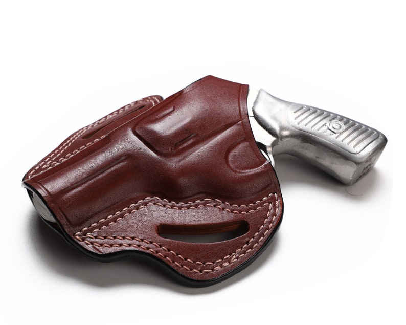 Puede incluir: Una funda de cuero marr&oacute;n con un rev&oacute;lver plateado en su interior. La funda tiene un dise&ntilde;o cosido y un recorte para la protecci&oacute;n del gatillo.