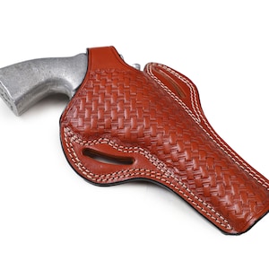 Może przedstawiać: Brązowa skórzana kabura z tkanym wzorem i białymi szwami. Kabura jest przeznaczona do przechowywania broni palnej.