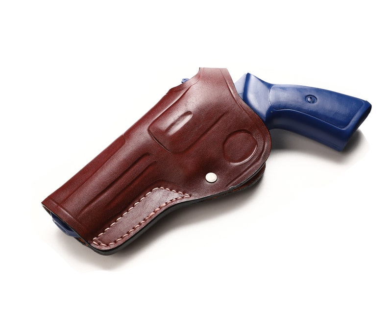 May include: A brown leather holster with a blue handgun inside. The holster has a flap that covers the trigger guard.