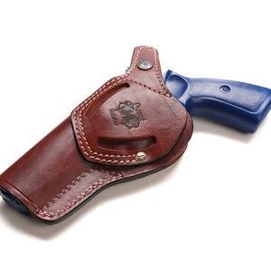 May include: A brown leather holster with a stitched design and a metal snap. A blue revolver is partially inside the holster.
