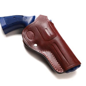 Op de afbeelding: Een bruin leren holster met een blauwe pistoolgreep. De holster heeft een gestikt ontwerp langs de randen en een zilveren klinknagel. Het pistool is gedeeltelijk zichtbaar en rust in de holster.