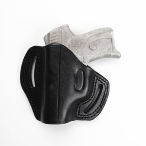 May include: Black leather holster with stitched detailing, designed to hold a handgun. The holster has a molded shape and features cutouts for belt attachment. A silver-colored handgun is partially visible.