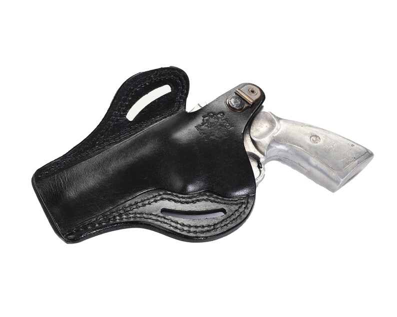 May include: A black leather holster for a revolver. The holster has a belt loop and a snap closure. The revolver is silver and has a wooden handle.