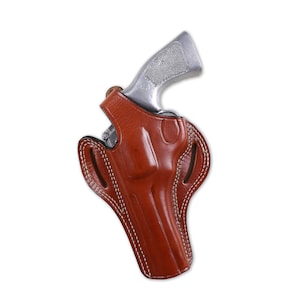 Könnte beinhalten: Ein braunes Lederholster mit weißen Nähten hält einen silbernen Revolver. Das Holster hat ein geformtes Design und besteht aus glattem, poliertem Leder. Der Revolver ist teilweise sichtbar.