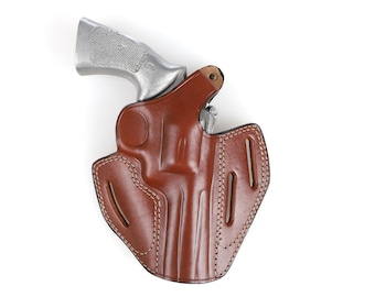 May include: A brown leather holster with a silver handgun. The holster has a stitched border and cutouts for a belt. The handgun's grip is visible, and the holster appears to be designed for a specific firearm model.