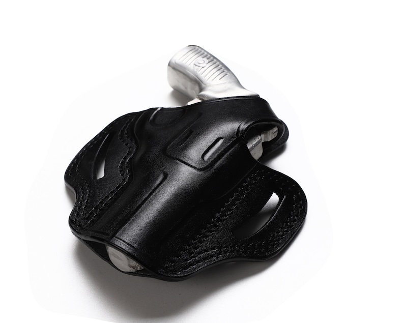 Puede incluir: Una funda de cuero negra para una pistola. La funda tiene un dise&ntilde;o cosido y un recorte para el guardamonte.
