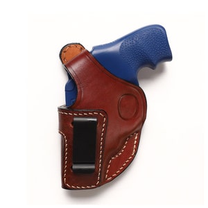 May include: A brown leather holster with a black clip for a blue handgun.