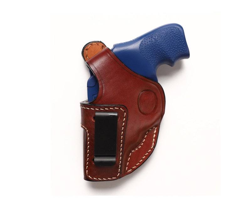 May include: A brown leather holster with a black clip for a blue handgun.