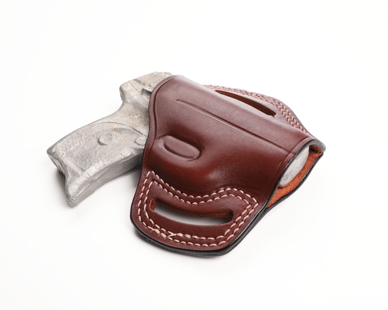 May include: A brown leather holster with white stitching, holding a silver-colored handgun. The holster has a molded design and is set against a white background. The stitching is visible along the edges and around the belt loops.