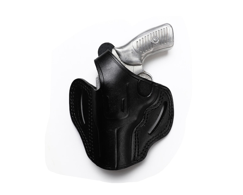 Puede incluir: Una funda de cuero negra con una pistola plateada en su interior. La funda tiene detalles de costura y un bucle para el cintur&oacute;n.