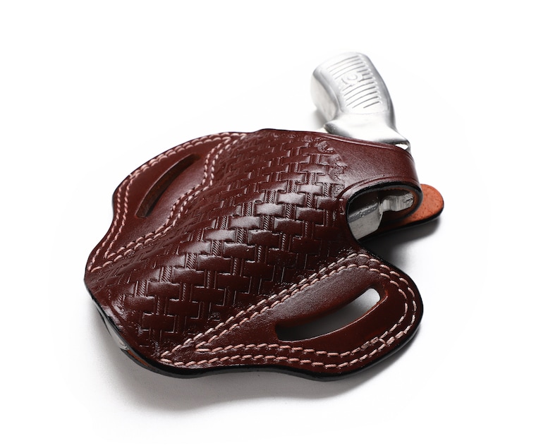 May include: A brown leather holster with a woven pattern and a silver handgun inside.