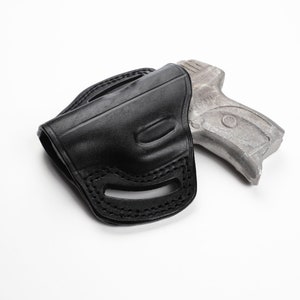 May include: A black leather holster with a stitched design, holding a silver-colored handgun. The holster has a molded shape and belt loops. The handgun is partially visible, resting inside the holster.