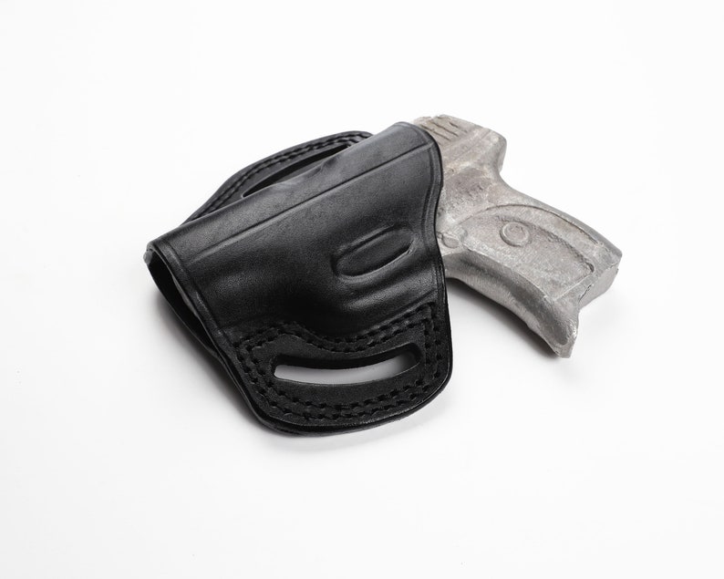 May include: A black leather holster with a stitched design, holding a silver-colored handgun. The holster has a molded shape and belt loops. The handgun is partially visible, resting inside the holster.