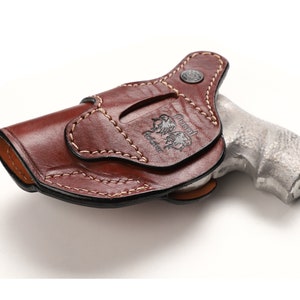 Puede incluir: Una funda de cuero marr&oacute;n con un dise&ntilde;o cosido y el texto "Russell Holster" grabado en relieve en el lateral. La funda est&aacute; dise&ntilde;ada para sujetar un rev&oacute;lver.