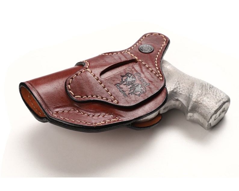Puede incluir: Una funda de cuero marr&oacute;n con un dise&ntilde;o cosido y el texto "Russell Holster" grabado en relieve en el lateral. La funda est&aacute; dise&ntilde;ada para sujetar un rev&oacute;lver.