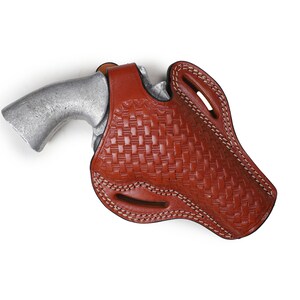 May include: A brown leather holster with a woven pattern and white stitching. A silver handgun is inside the holster.