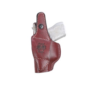 以下が含まれることがあります： 側面に「Pusat Holster」という文字が刻印された、ステッチデザインのブラウンレザーホルスターです。