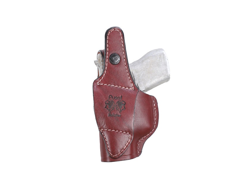 以下が含まれることがあります： 側面に「Pusat Holster」という文字が刻印された、ステッチデザインのブラウンレザーホルスターです。