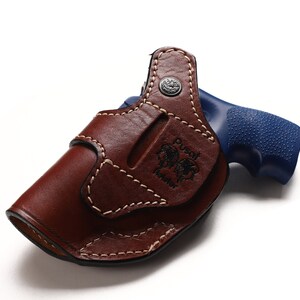 May include: A brown leather holster with a stitched design and the text "Dust Devil Holster" embossed on the side. A blue handgun is partially visible in the holster.