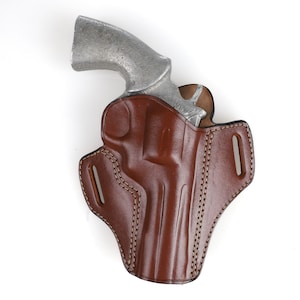 May include: A brown leather holster with a silver revolver inside. The holster has stitching around the edges and a belt loop.