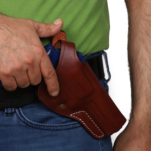 May include: A brown leather holster with a blue gun inside. The holster is attached to a belt and is worn on the right side of the body.
