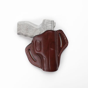 Puede incluir: Una funda de cuero marr&oacute;n con un dise&ntilde;o cosido y una pistola en su interior.