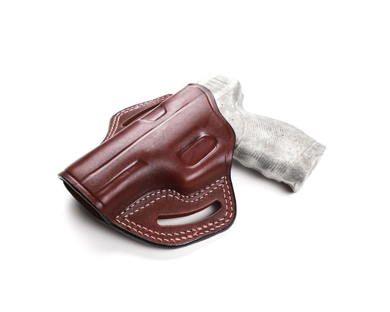 Puede incluir: Una funda de cuero marr&oacute;n con un dise&ntilde;o cosido para una pistola. La funda est&aacute; vac&iacute;a y el arma no es visible.