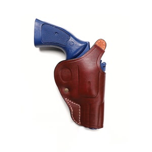 Könnte beinhalten: Eine blaue Revolverpistole in einem braunen Lederholster. Das Holster hat ein genähtes Design und einen Messingknopf.